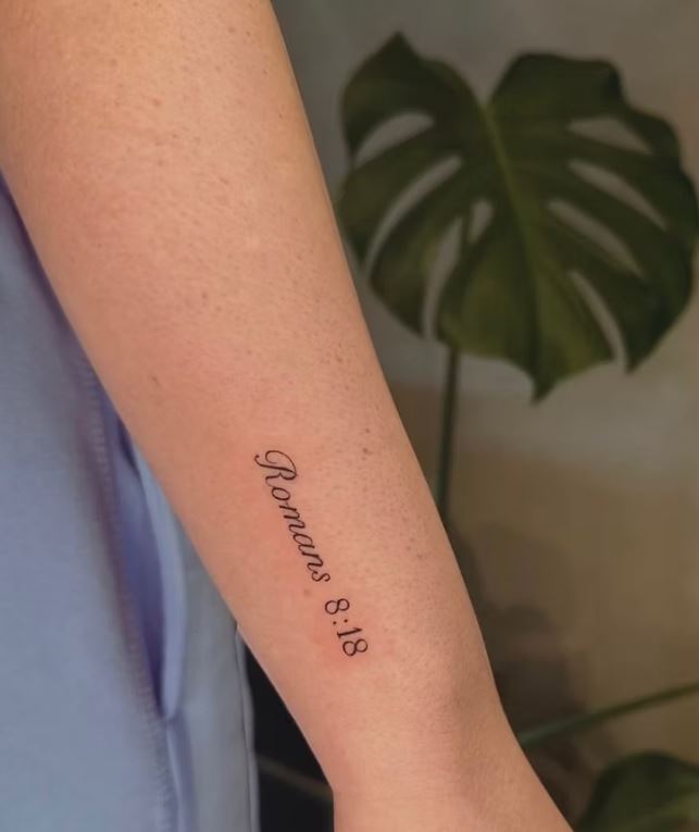 "Romans 8:18" script tattoo on forearm