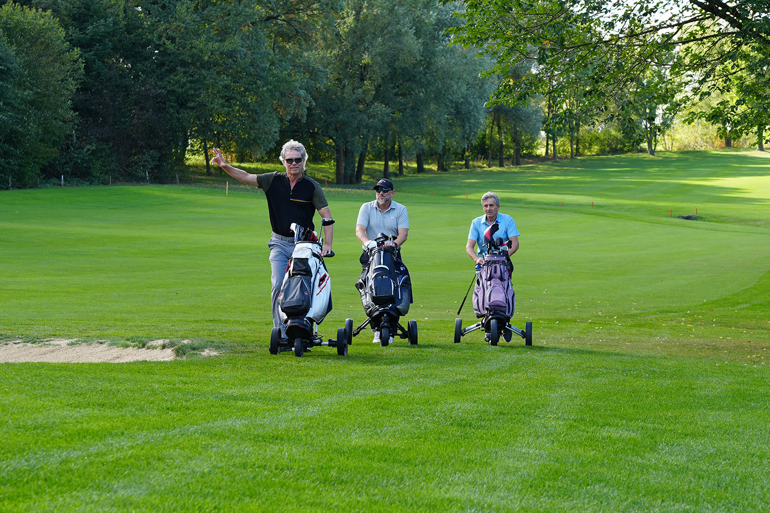 Drei Spieler mit Golf-Trolleys auf dem Platz