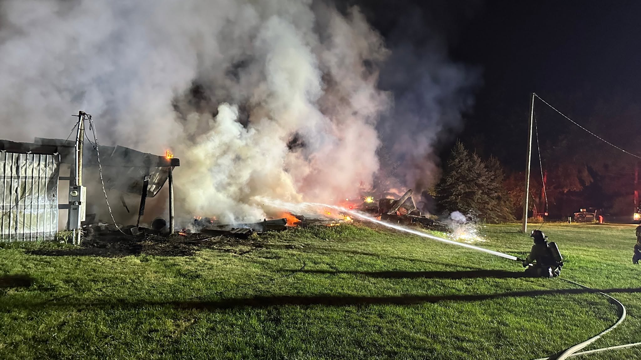 Firefighter directing a hose stream into a burning structure at night.