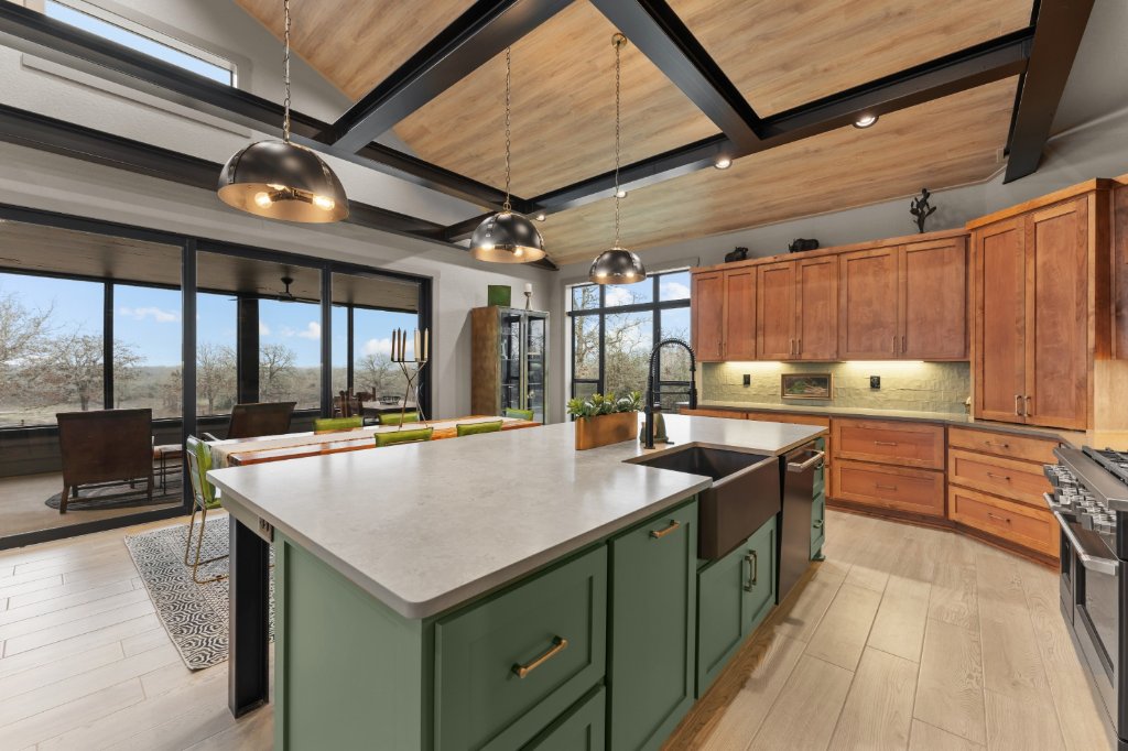 Sage green kitchen island with farmhouse sink and natural wood cabinets by CJ Cabinets