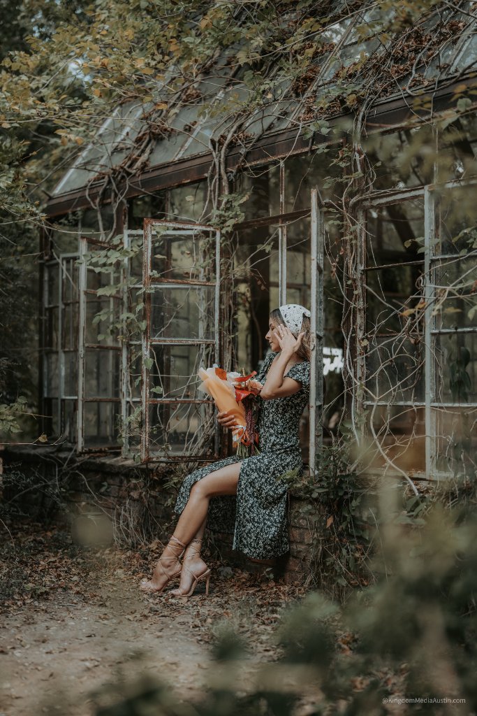 Bride sitting on greenhouse ledge with bouquet