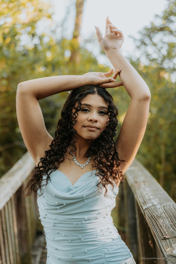 Quinceañera in light blue gown with arms raised on a bridge