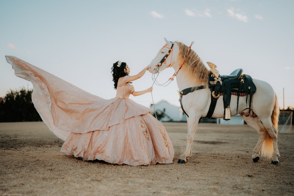 Quinceañera in champagne gown reaching toward a white horse