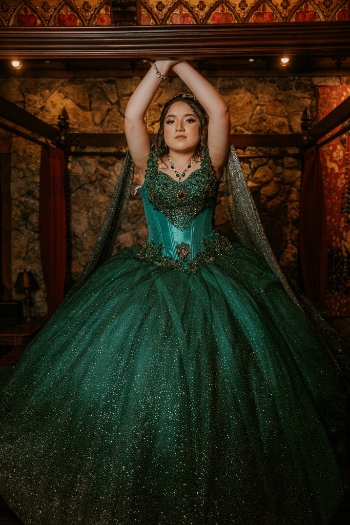 Quinceañera in emerald green gown inside a stone room