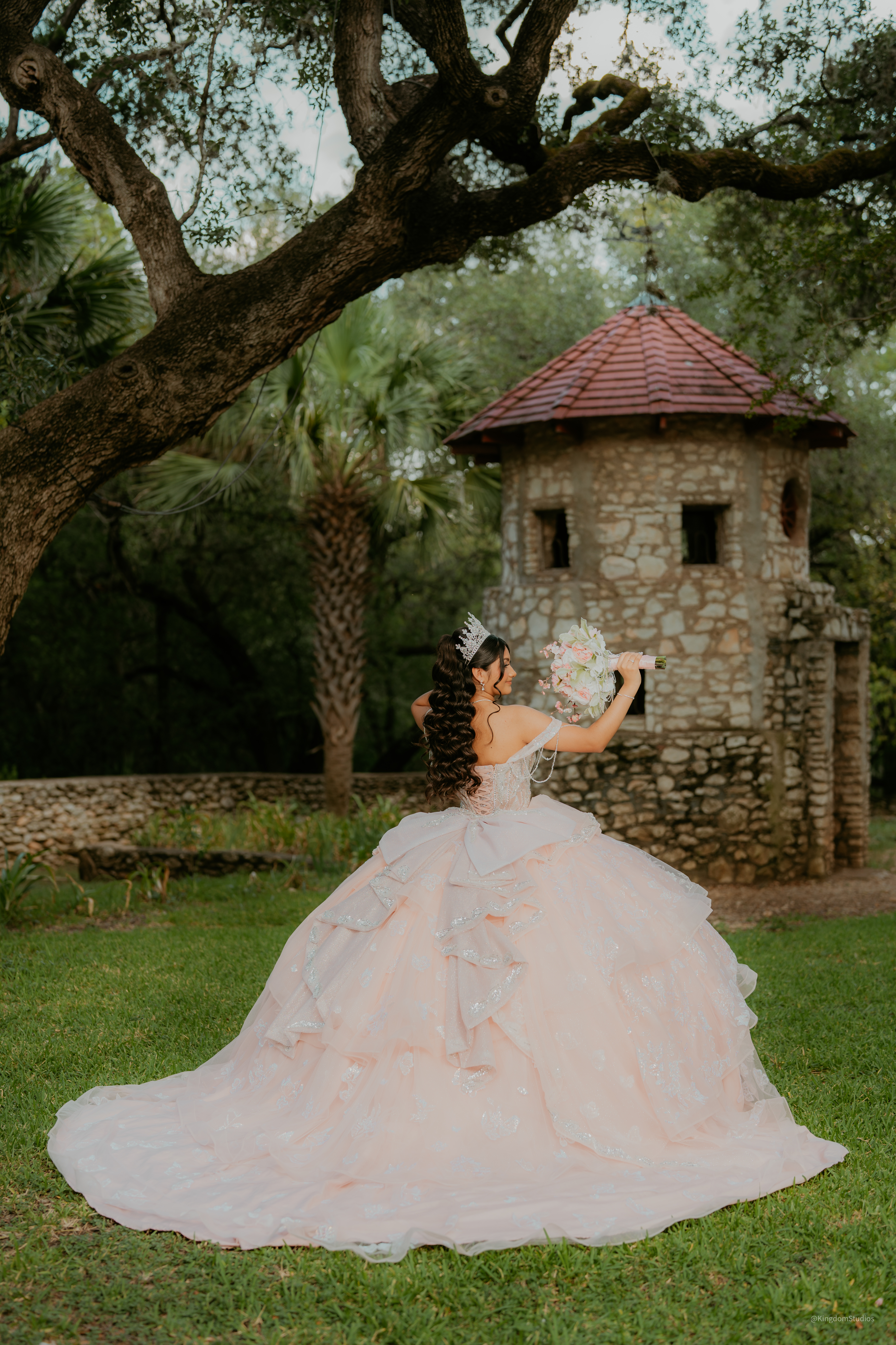Quinceañera in pale pink gown looking back over her shoulder holding a bouquet