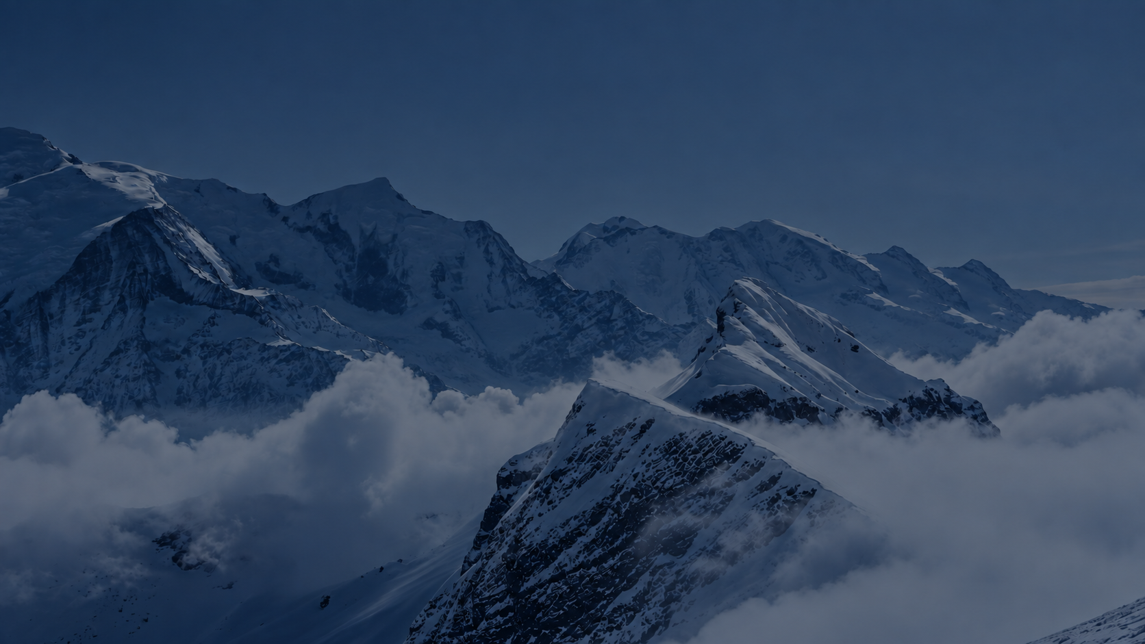 Snow-covered mountain peaks above a sea of clouds at twilight