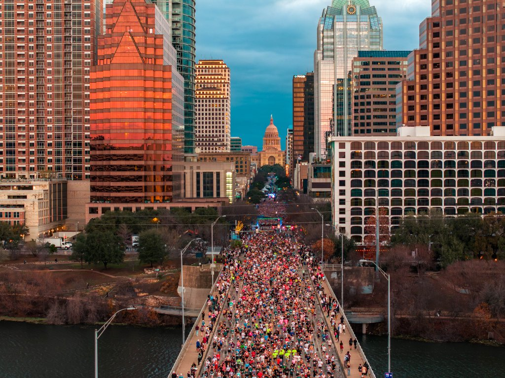 Thousands of marathon runners crossing a bridge at dawn in Austin