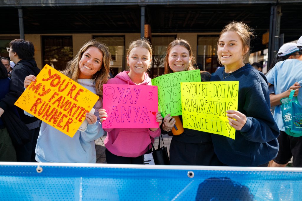Four women holding colorful motivational signs for a runner