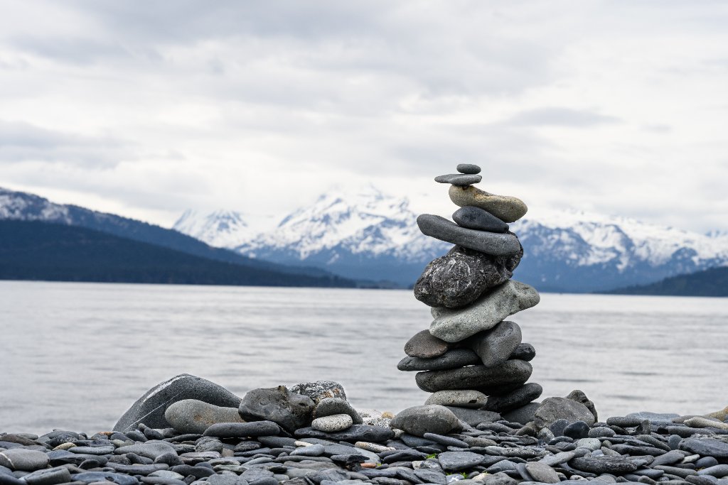 Stone cairn balancing on a frozen lake with snow-capped mountains in the background
