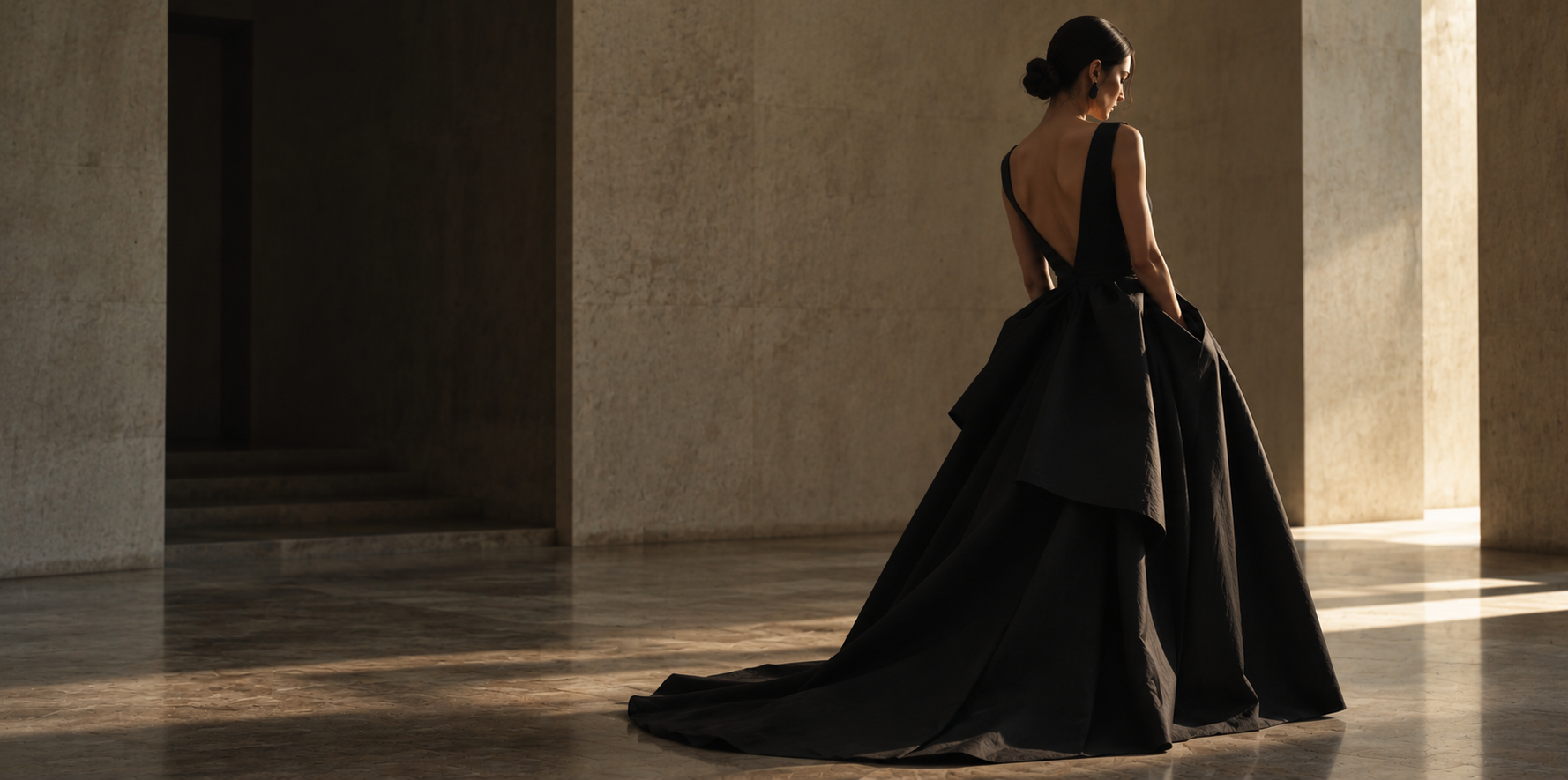 A woman in a black floor-length gown within a minimalist architectural hall
