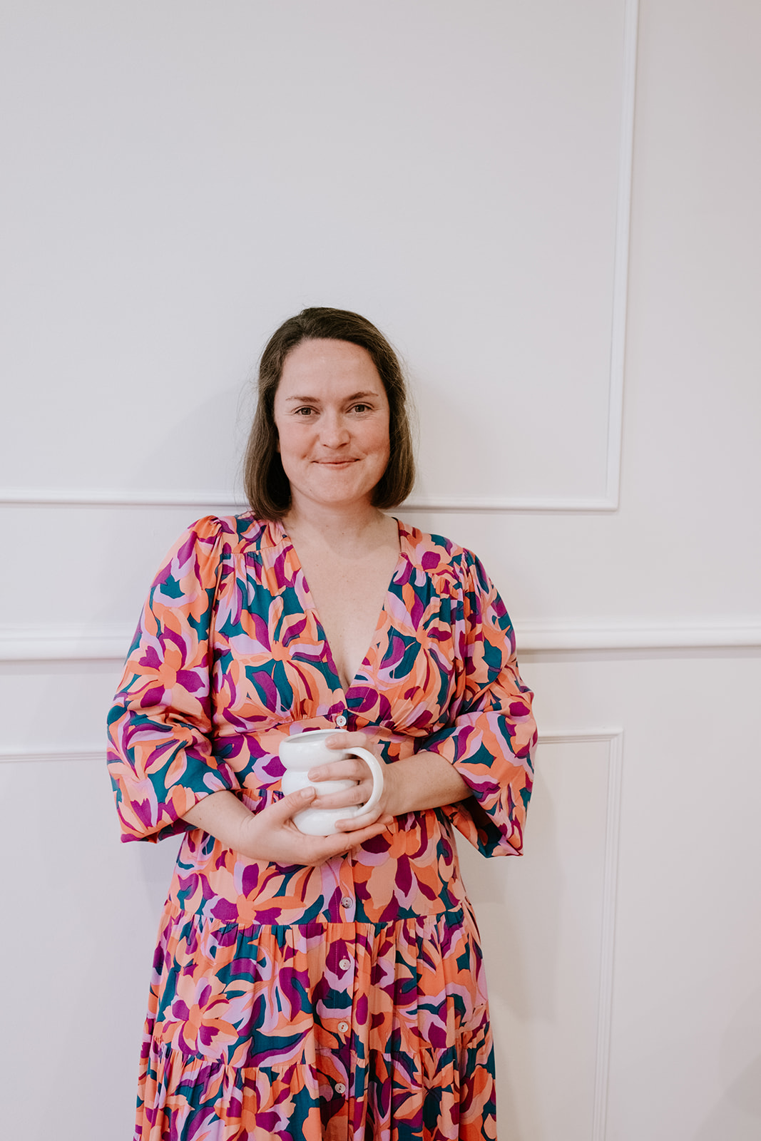 Shelly, founder of Rise, holding a mug in a vibrant floral dress