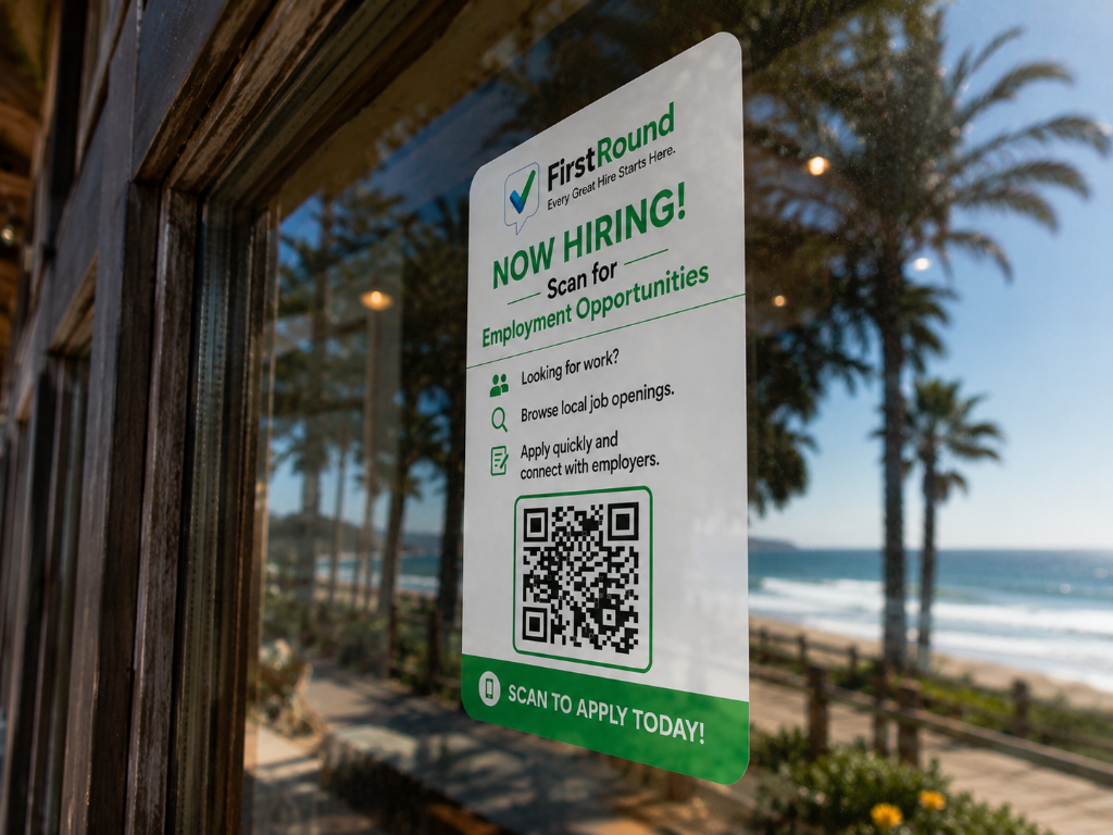 FirstRound NOW HIRING sign in a beachfront window overlooking palm trees and the ocean