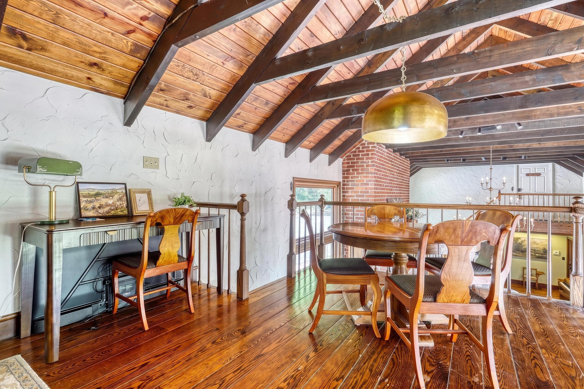 Loft dining nook with round wooden table, brass pendant light, and exposed beamed ceiling