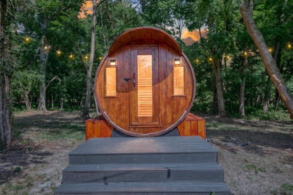 Wooden barrel sauna glowing at twilight among the trees