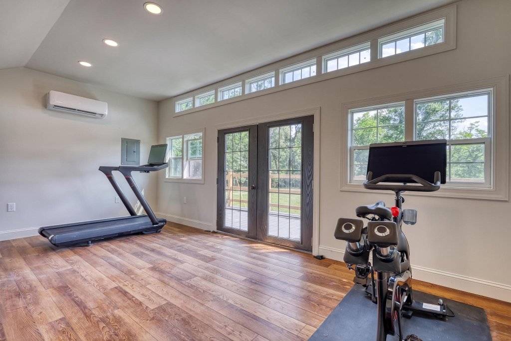 Bright fitness center with treadmill, bike, and French doors to the deck