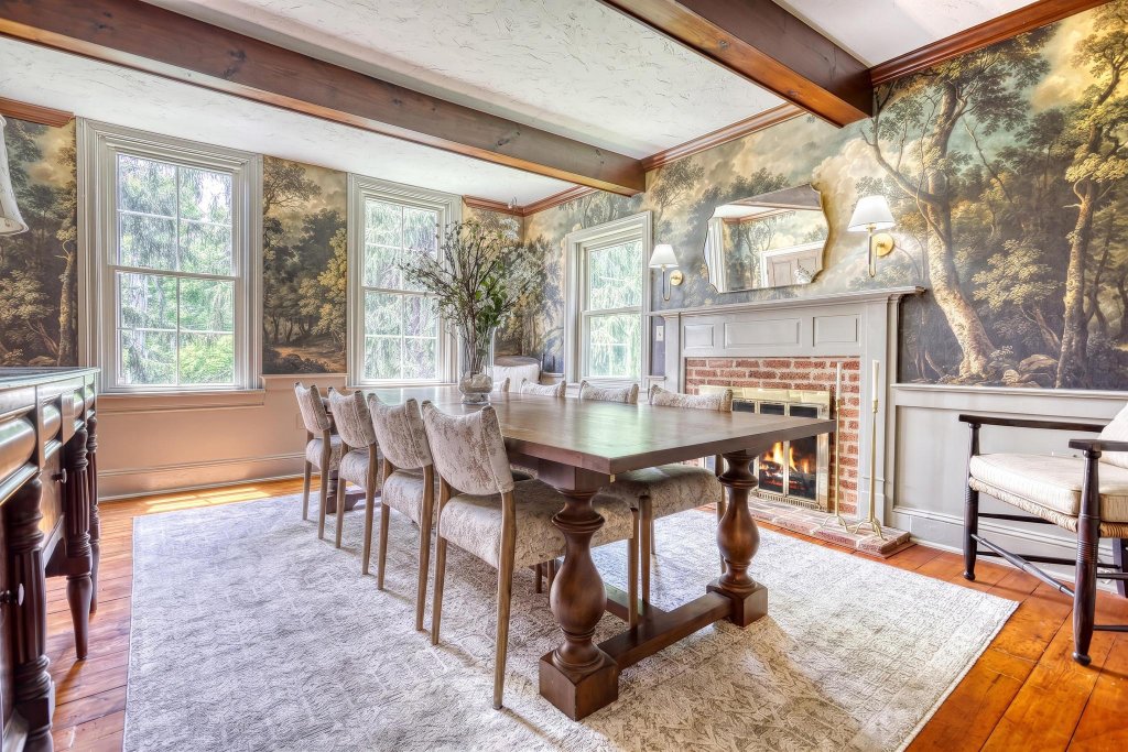 Elegant dining room with a long wooden table, mural wallpaper, and a lit fireplace
