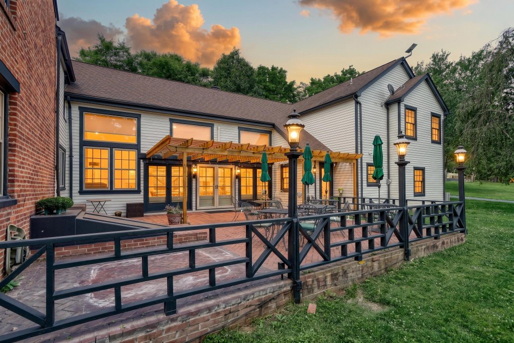 The Patio at twilight, furnished with dining tables under a pergola overlooking the lawn