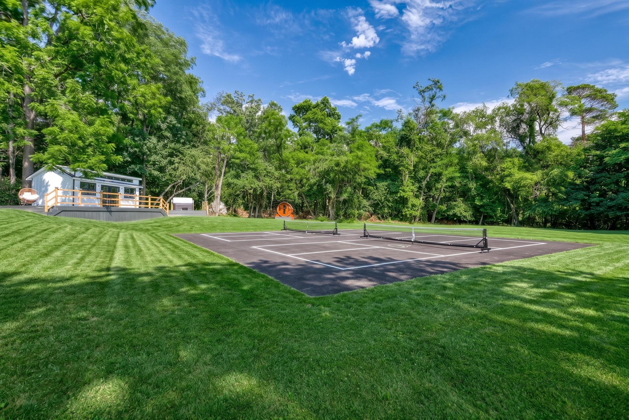 The Courtyard — an open lawn with a pickleball court, framed by trees and a white building with a deck