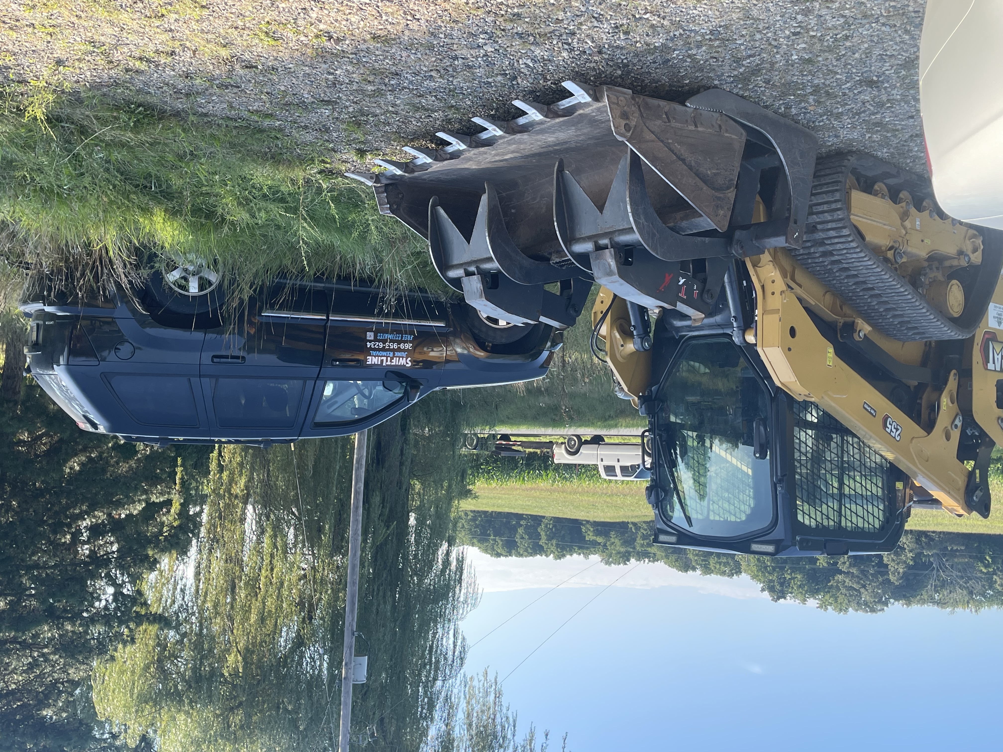 SwiftLine Junk Removal's branded truck and CAT skid steer loader with grapple bucket on-site, ready to haul away junk for a customer in Hastings, Michigan