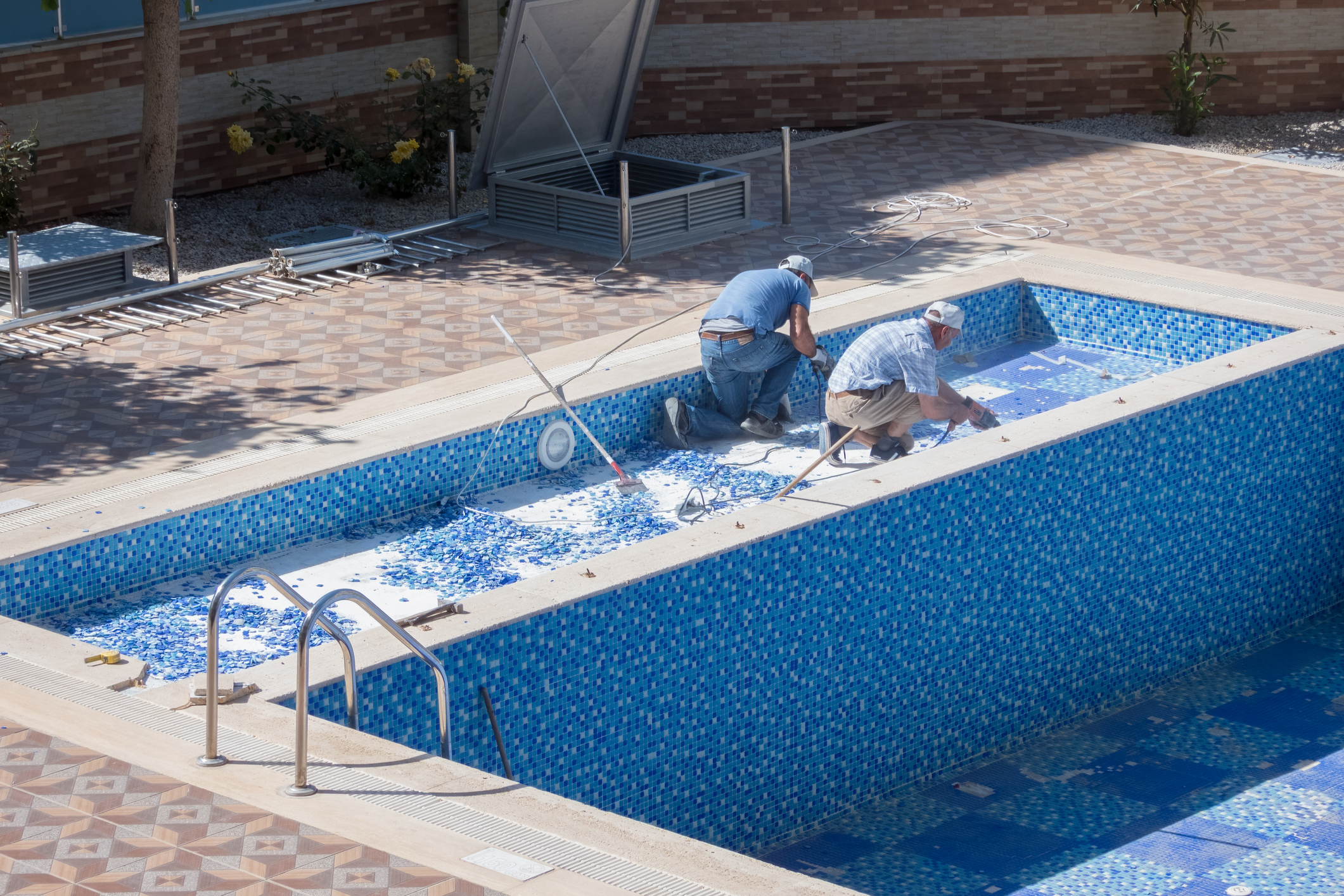 Two California Pools craftsmen setting blue mosaic tile inside a pool