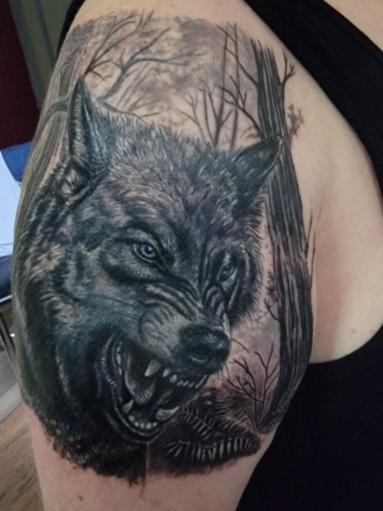 Snarling wolf with blue eyes in forest scene tattoo by Steve Gagliano
