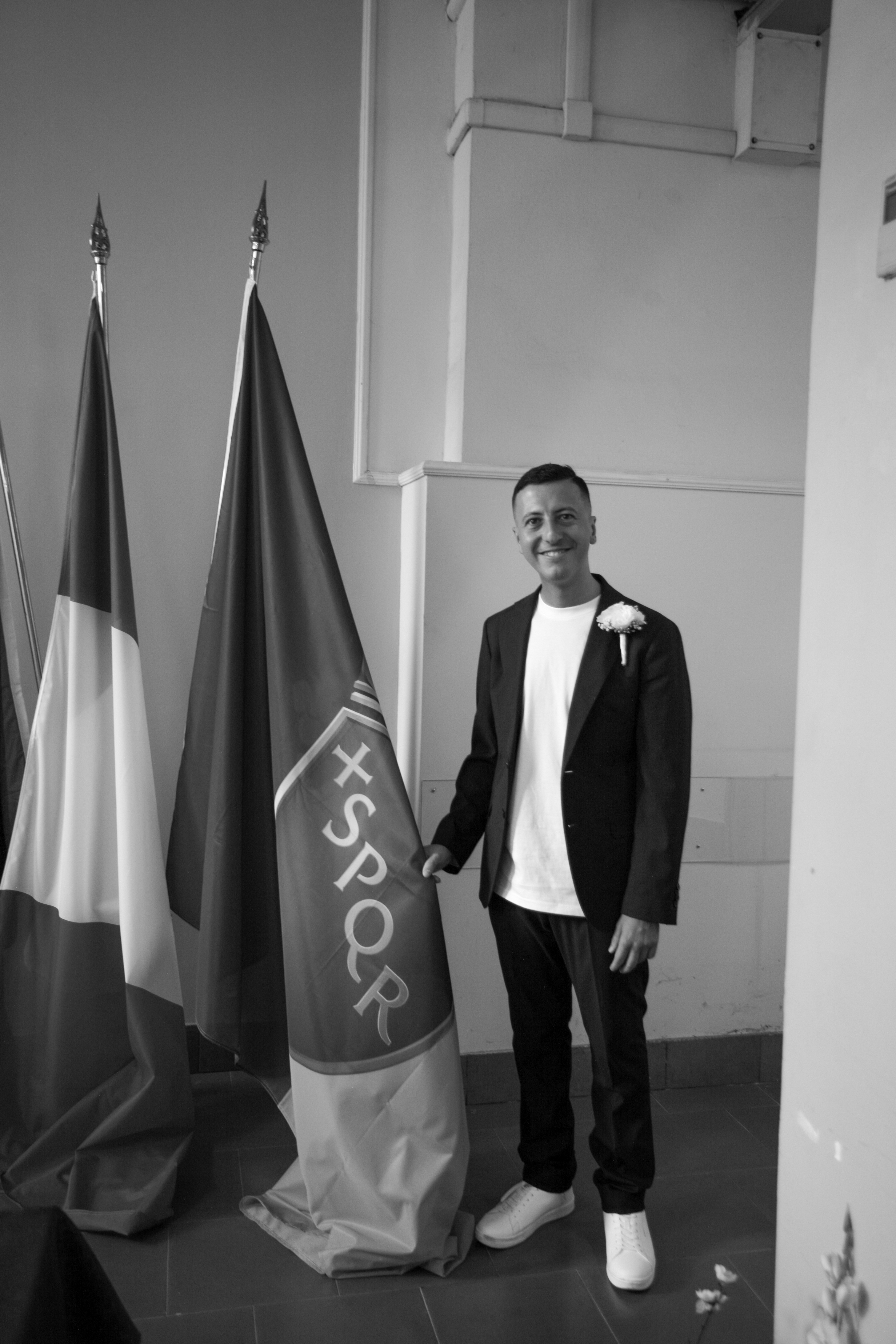 Emanuele in completo scuro tra le bandiere italiana e SPQR