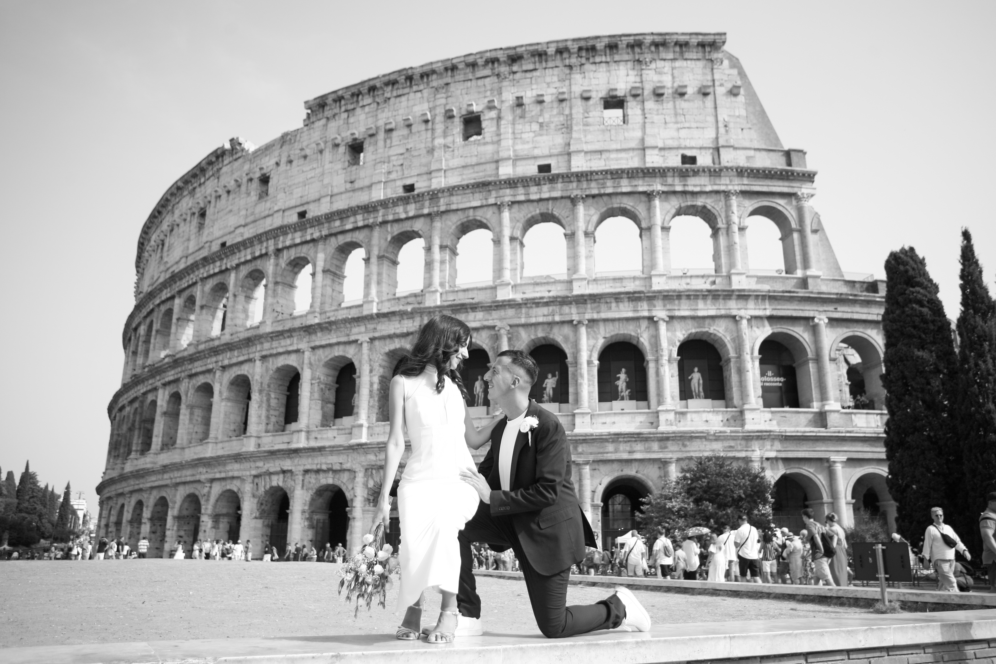 Lui in ginocchio davanti a lei seduta, con il Colosseo alle spalle