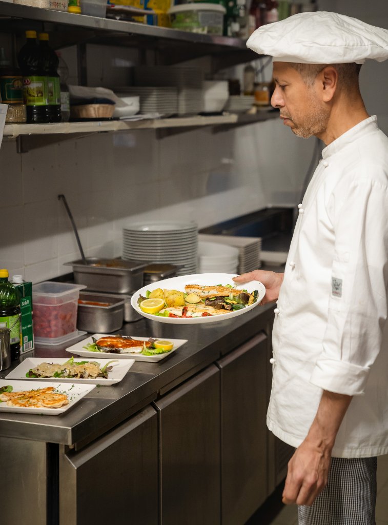 Chef holding a plated fish dish in the kitchen