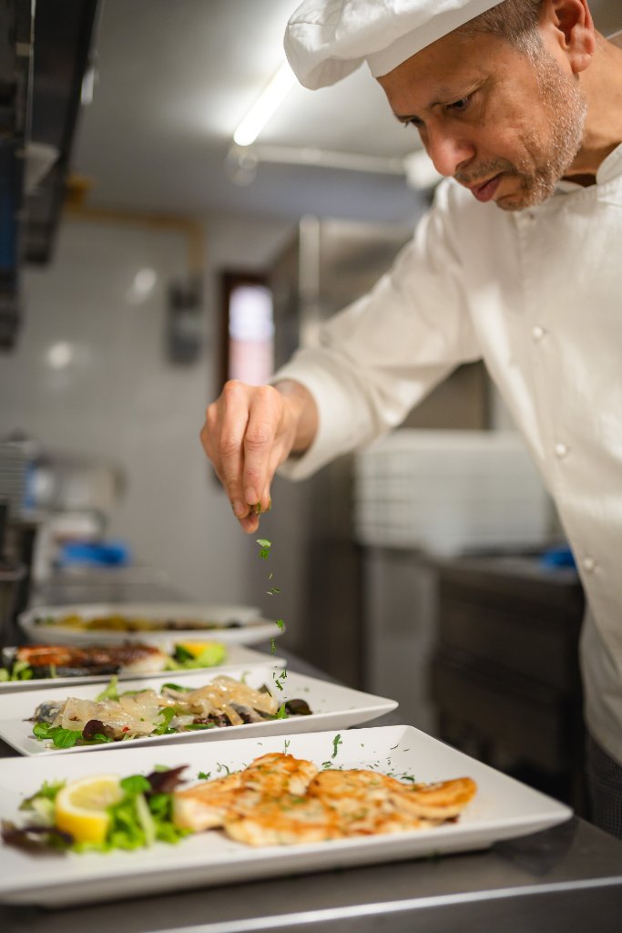 Chef sprinkling herbs over plated dishes