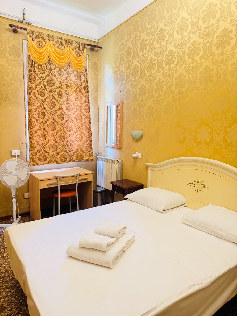 Gold damask wallpapered hotel room with double bed and ornate curtains