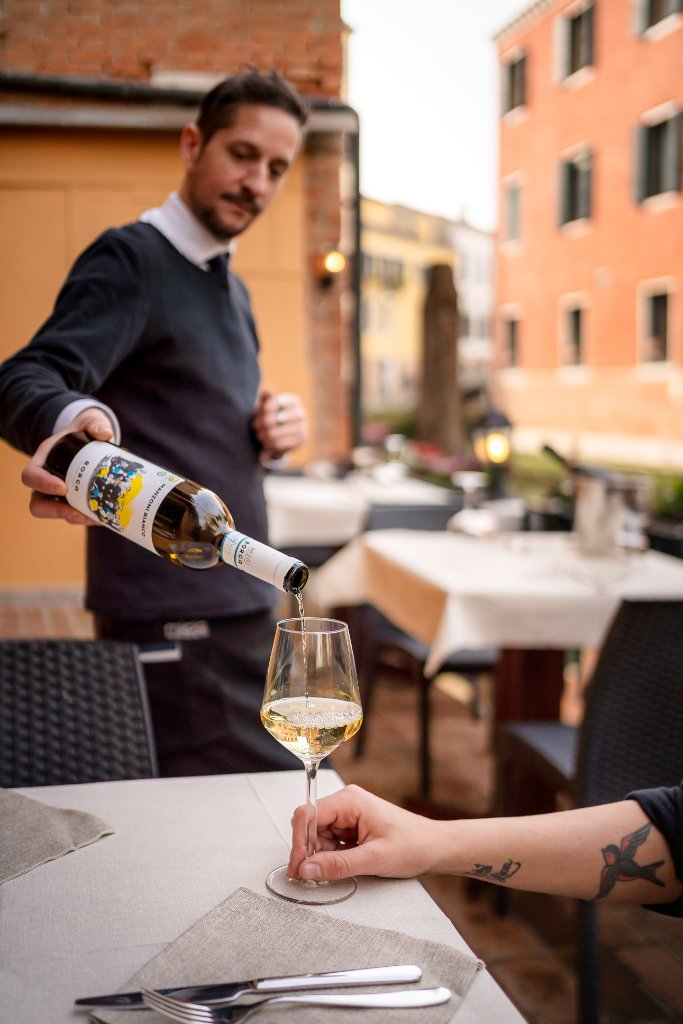 Waiter pouring white wine at a canal-side table
