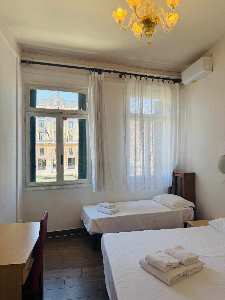 Hotel room with beds, desk and canal view through sheer curtains