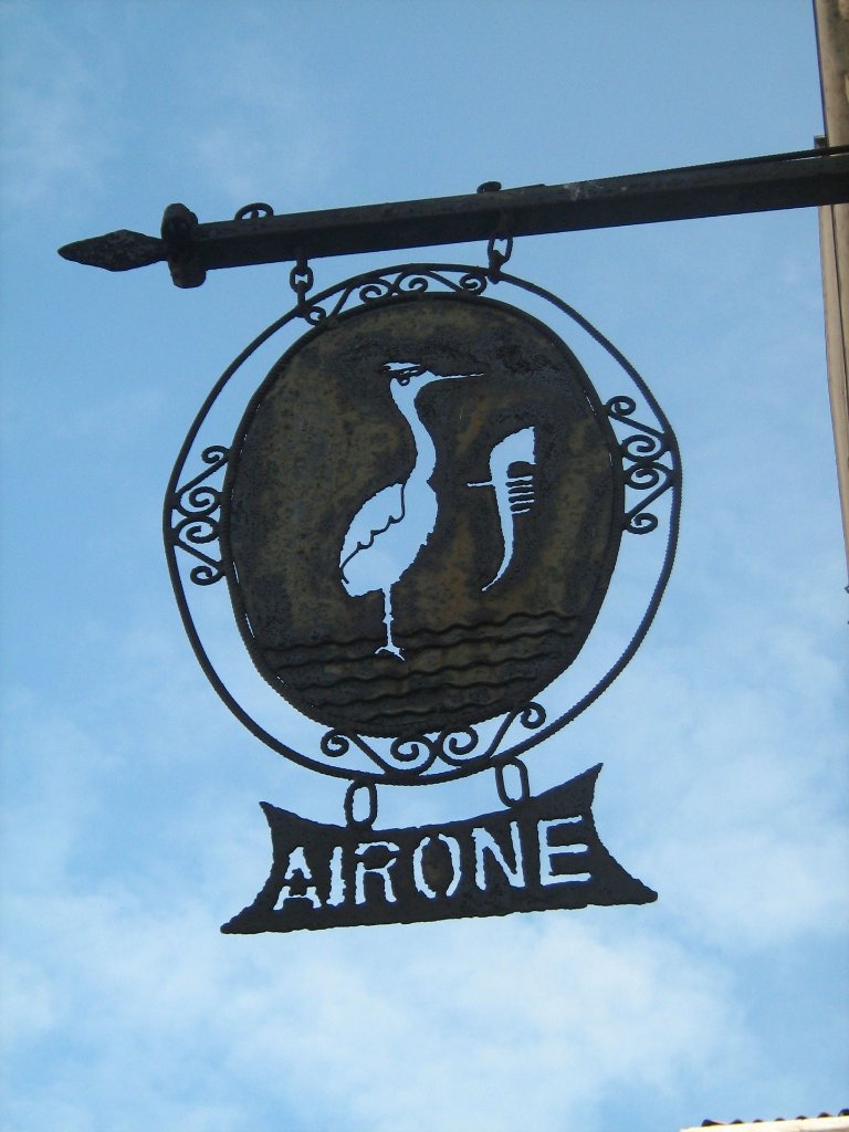 Ornate wrought-iron hanging sign of Hotel Airone with heron silhouette against blue sky