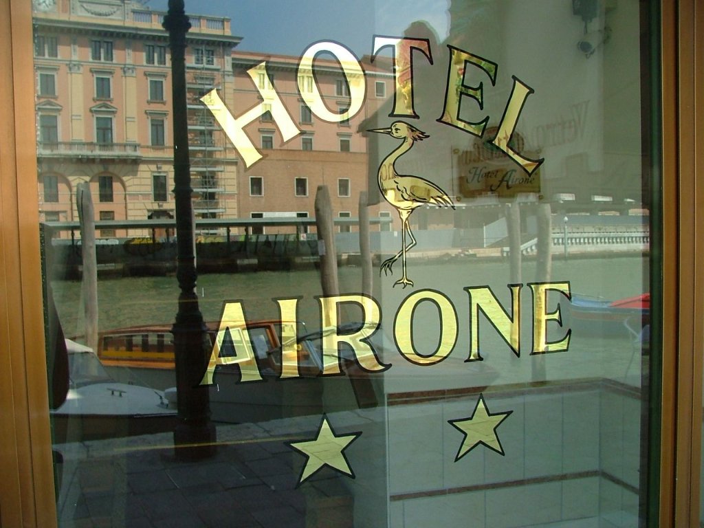 Hotel Airone gold signage with heron logo and two stars, seen through glass