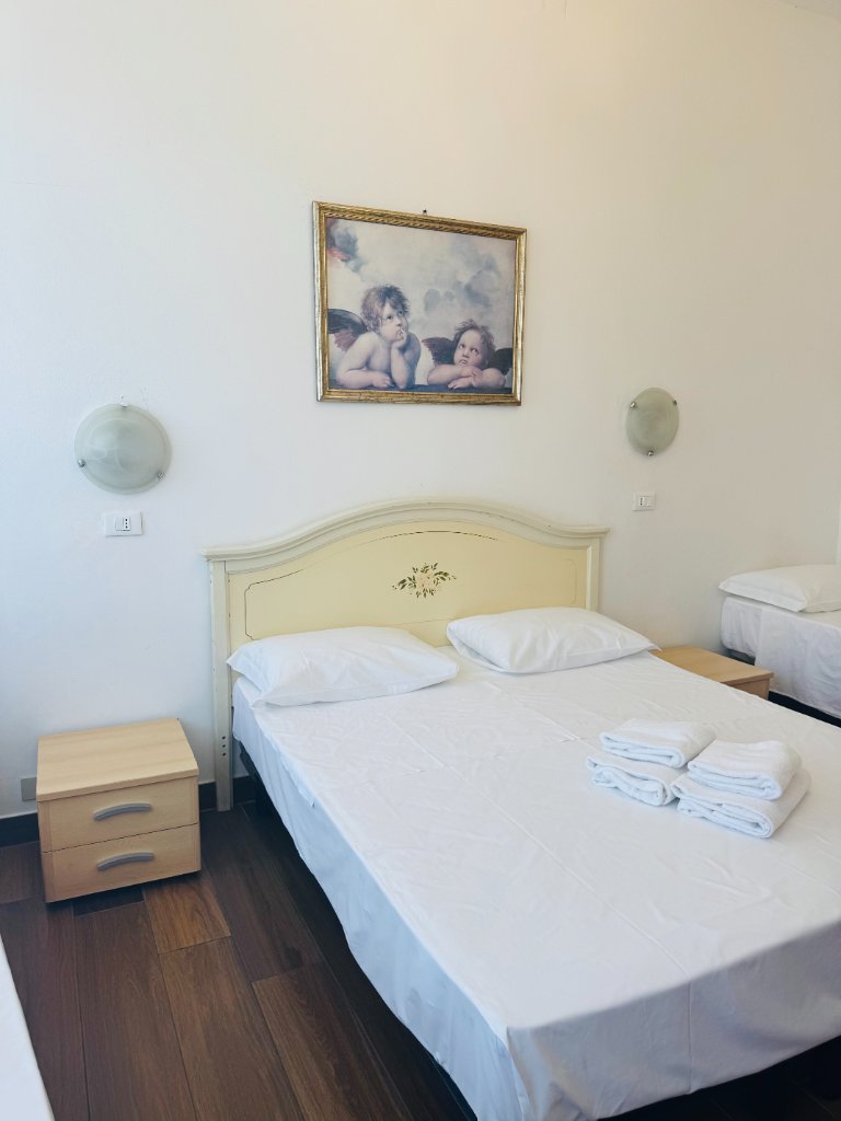 Double Room with Shared Bathroom featuring a double bed with cream headboard, white bedding, folded towels, and a framed cherub picture above