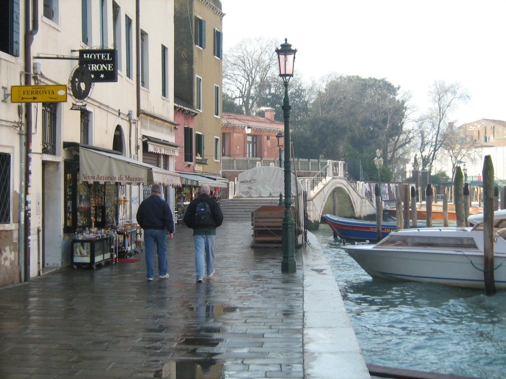 Stone path along a Venice canal with Hotel Airone hanging sign and moored boats