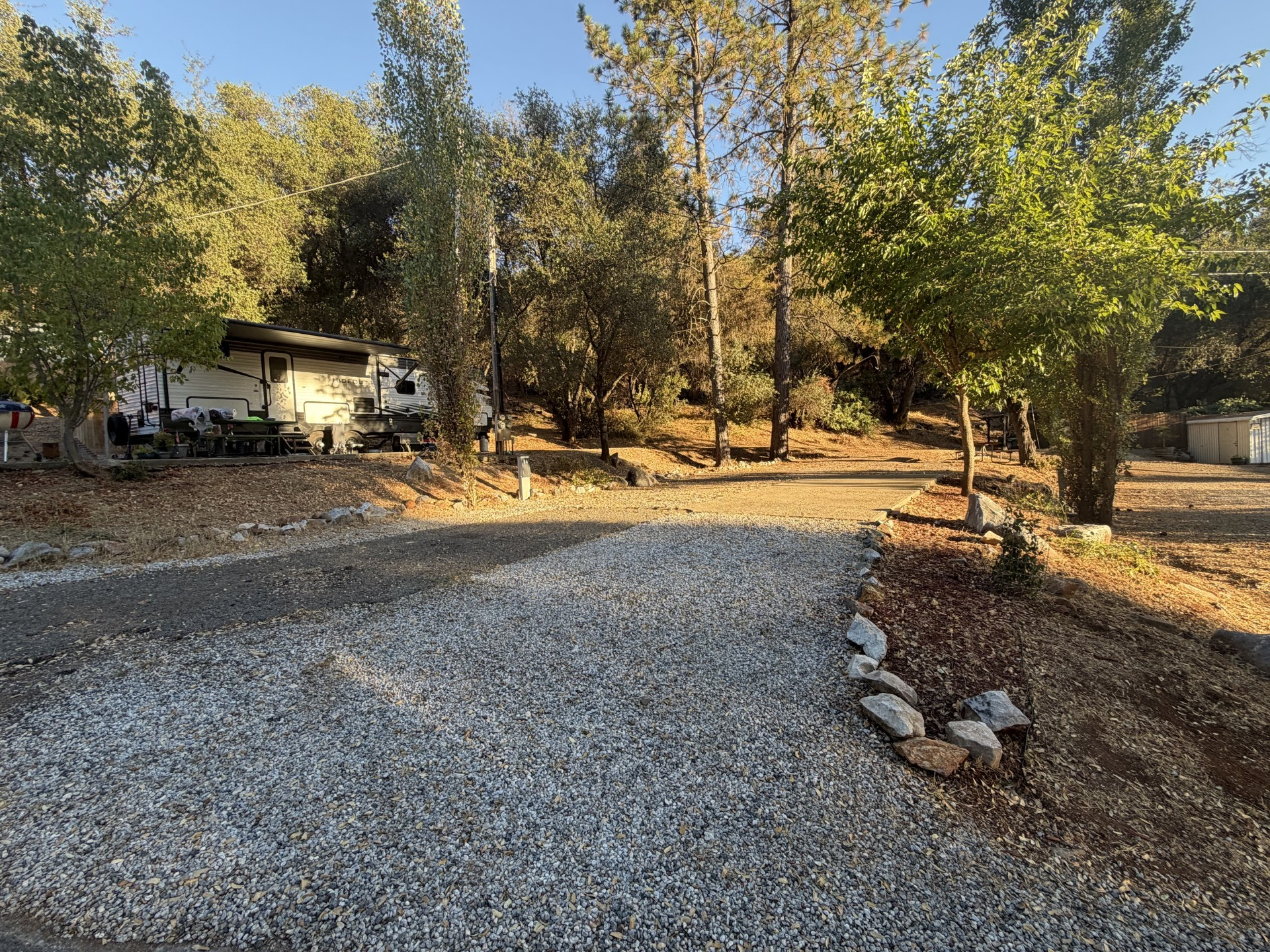 RV with its awning extended on a graveled pad beneath the oaks at Marble Quarry RV Resort