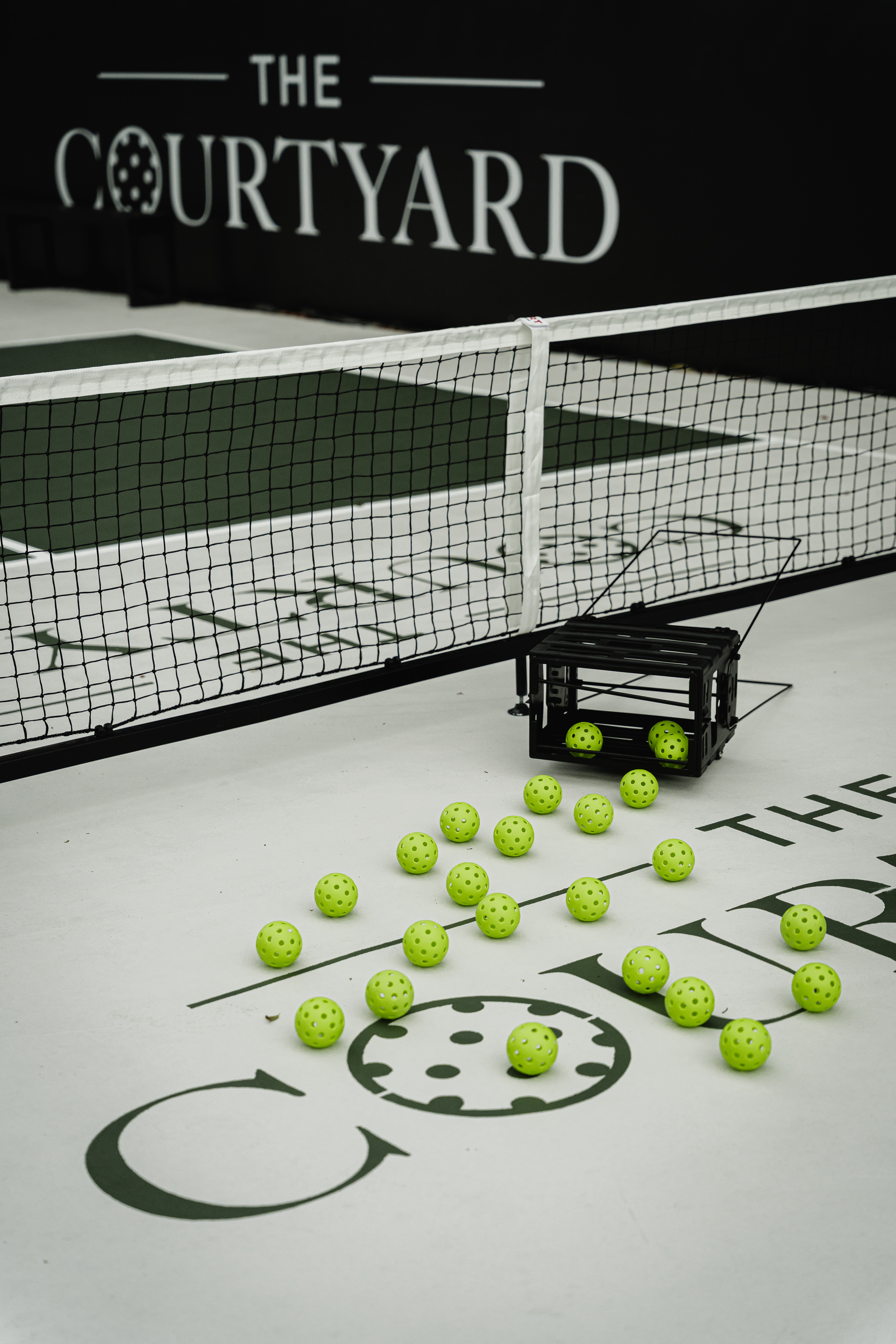Pickleballs arranged on court next to a ball crate in front of the net