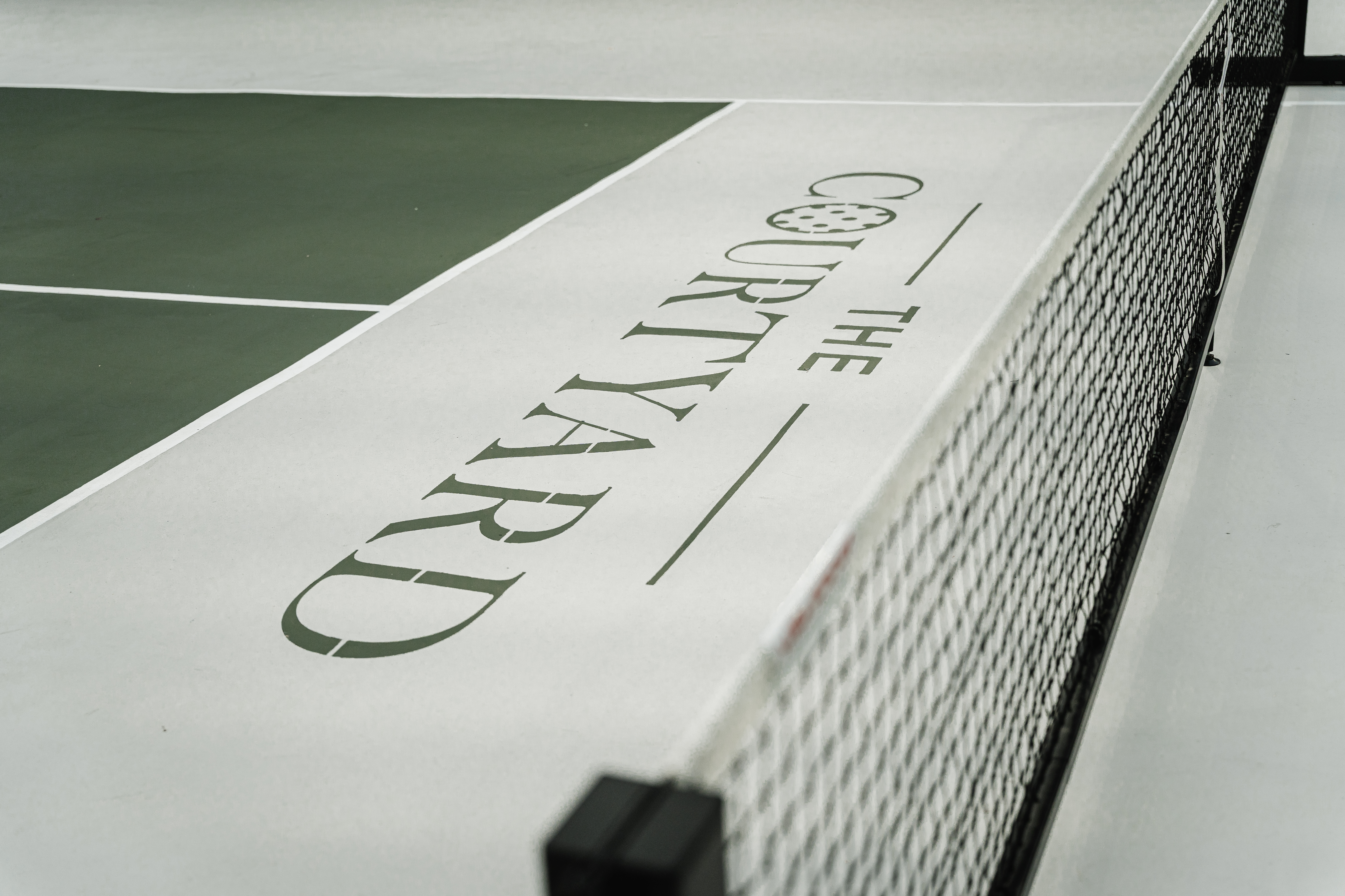 Close-up of The Courtyard logo stencilled on the court surface beside the net