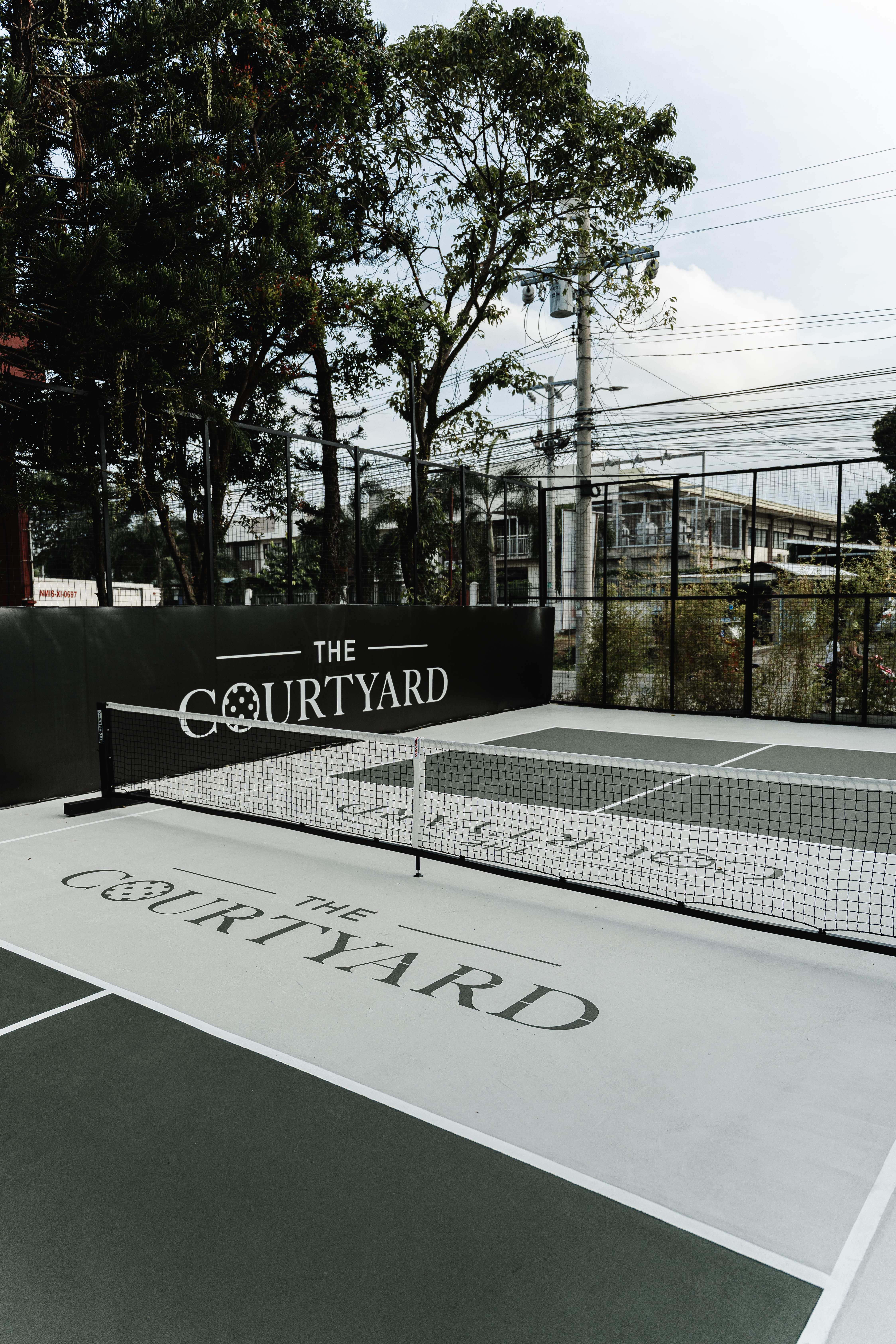 Wide view of a Courtyard pickleball court with trees and the branded perimeter wall