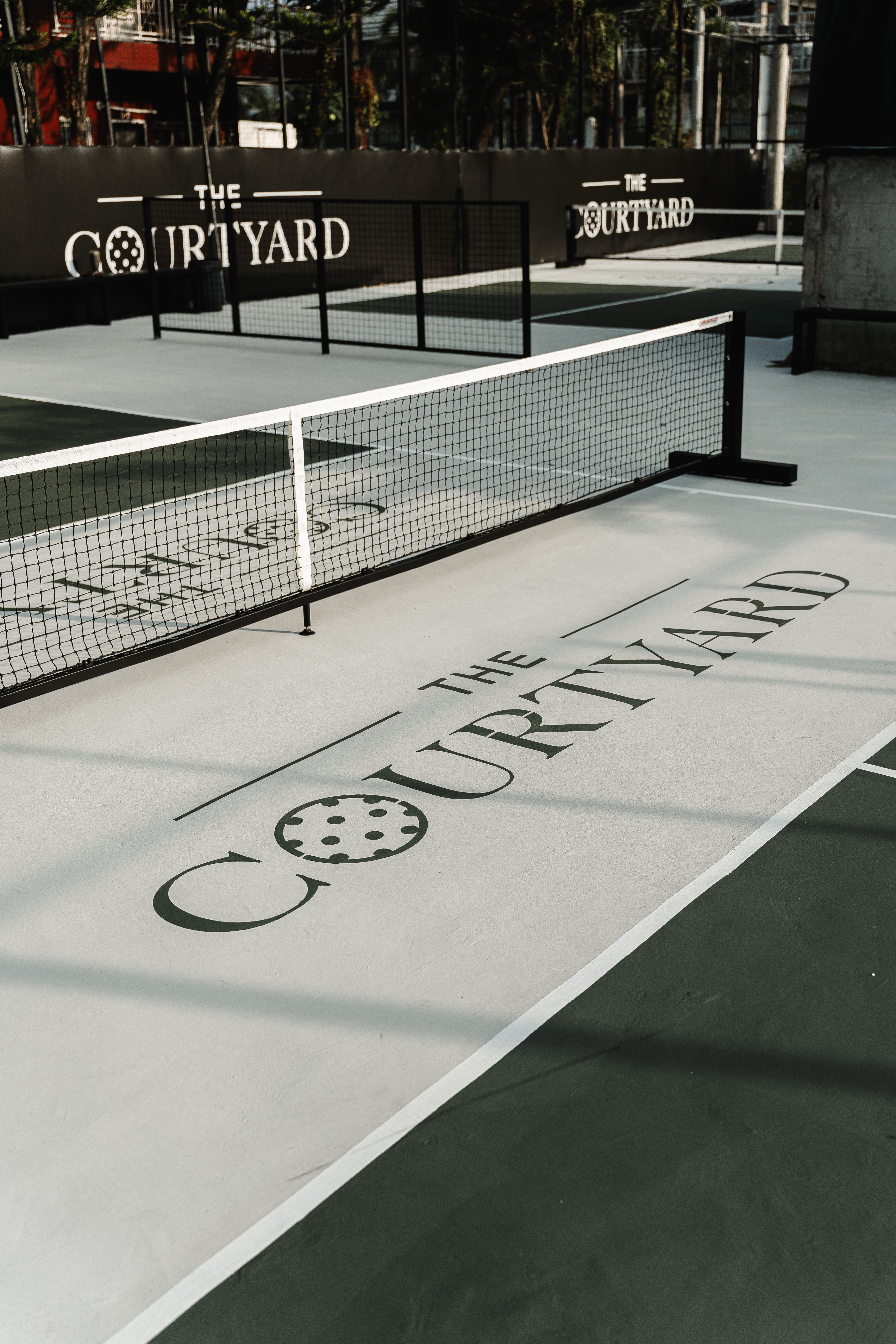 The Courtyard logo painted on the court surface beside the net, with branded walls behind