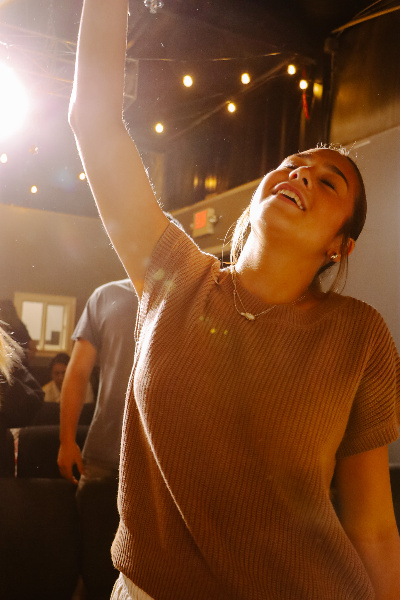 A woman worshiping with her arm raised under string lights