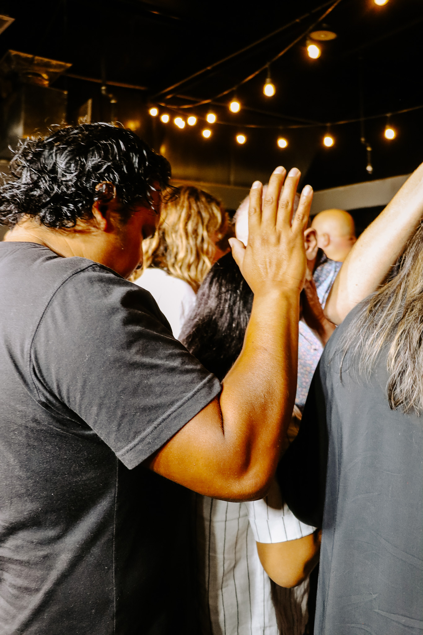 Arms raised in worship under Edison bulbs