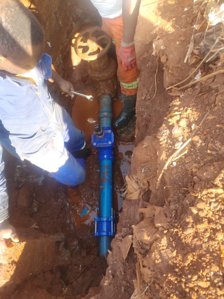Plumber tightening blue valve fitting in excavated trench