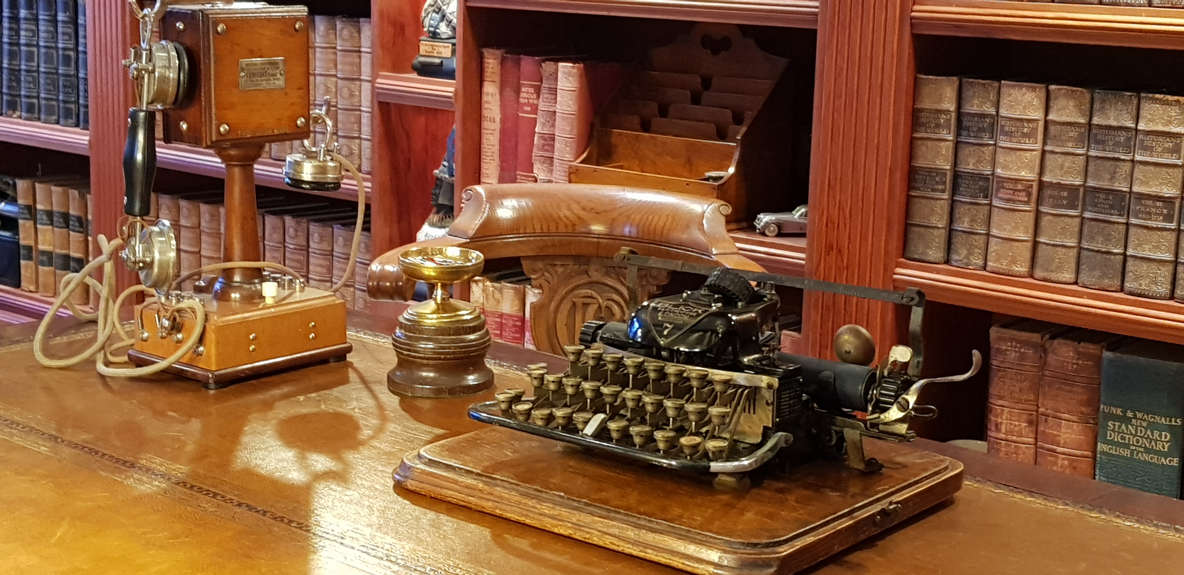Vintage study desk with a pedestal telephone and typewriter before bookshelves