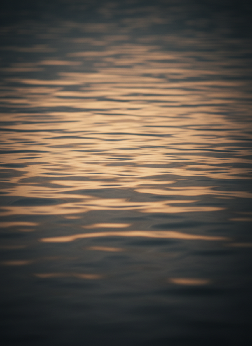 Calm water surface with amber light reflecting on dark water