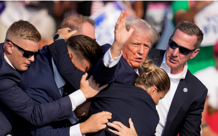 Donald Trump with blood running down face being escorted off stage Butler Pennsylvania July 13 2024