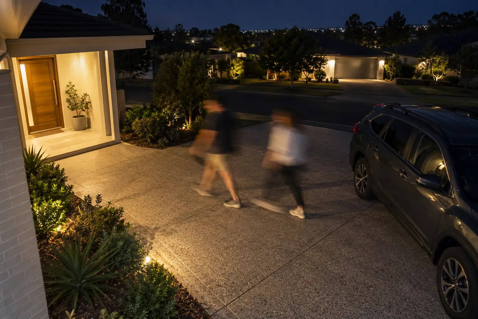 Motion-blurred figures walking across a driveway at night on security camera footage