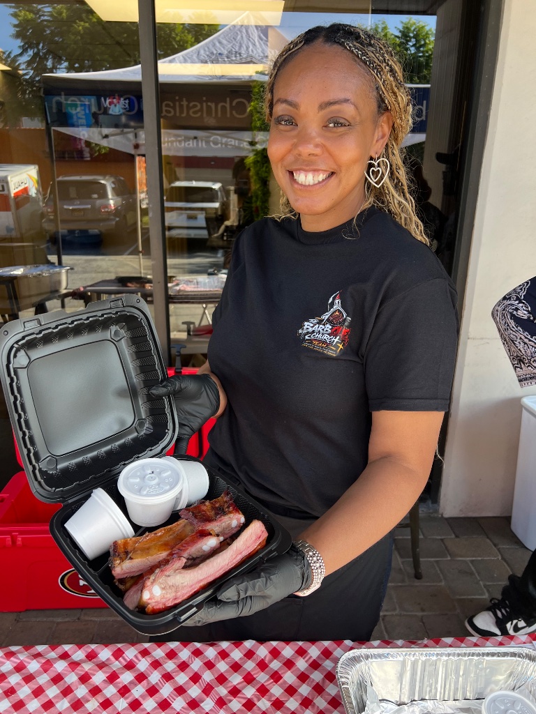 Team member holding an open container of barbecued ribs