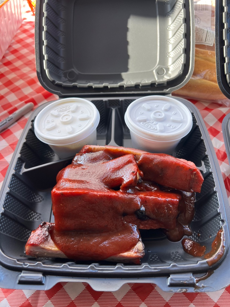 BBQ ribs and sides in a takeout container on a checkered tablecloth